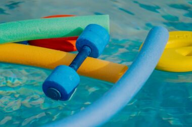 bunte Aquafitnessgeräte wie Poolnudeln und Hanteln schwimmen auf dem Wasser