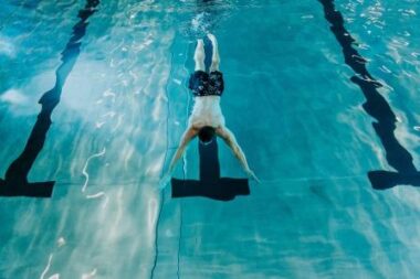 Mann in dunkler Badehose taucht eine Bahn im Rolli-Bad