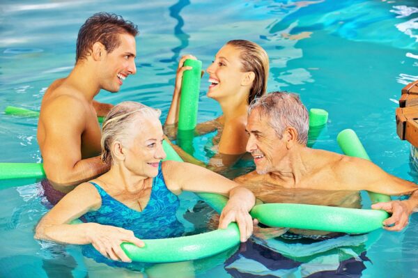 ein junges und ein älteres Paar mit Poolnudeln im Schwimmbecken