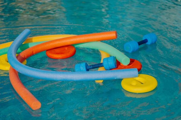bunte Aquafitnessgeräte wie Poolnudeln und Hanteln schwimmen auf dem Wasser